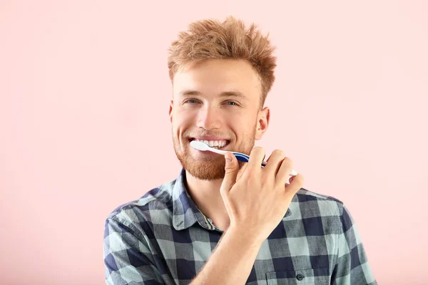 Mladý muž čištění zubů na barevném pozadí — Stock fotografie