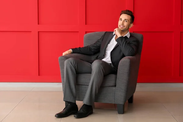 Knappe zakenman zit in fauteuil in de buurt van kleur muur — Stockfoto