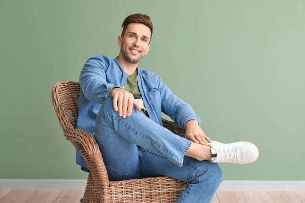 Handsome man sitting in armchair near color wall — Stock Photo, Image