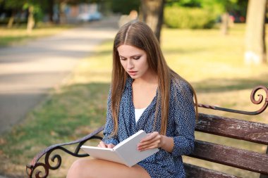 Parkta kitap okuyan güzel genç bir kadın.