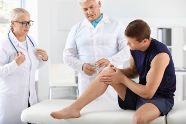 Klinikte eklem ağrısı olan sporcuyu muayene eden olgun doktorlar.
