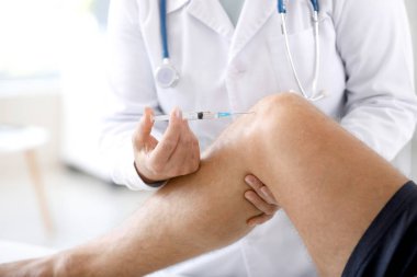 Doktor klinikte eklem ağrısı iğnesi ile sporcuya yakın çekim yapıyor.