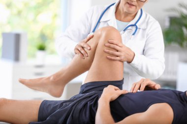 Mature doctor examining sportsman with joint pain in clinic