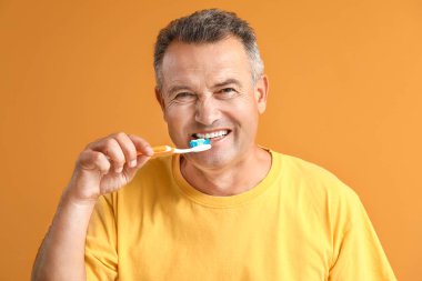 Renkli arka planda dişlerini fırçalayan olgun bir adam