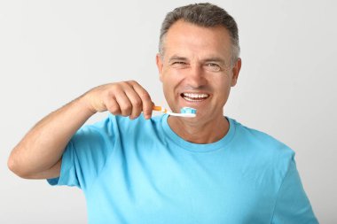 Olgun bir adam arka planda dişlerini fırçalıyor.