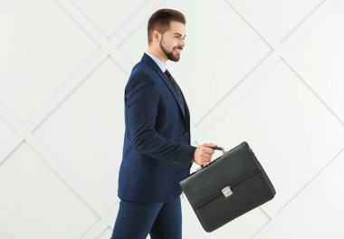 Gri arka planda çantası olan yakışıklı iş adamının portresi.