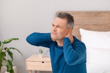 Yatak odasında boynu ağrıyan olgun bir adam.