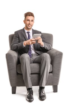 Tablet bilgisayarı olan yakışıklı iş adamı beyaz arka planda koltukta oturuyor.