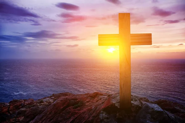 Skała z chrześcijańskim krzyżem w pobliżu morza o zachodzie słońca — Zdjęcie stockowe