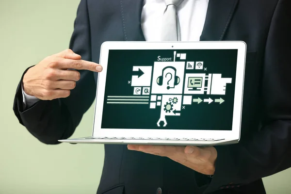 Businessman pointing on icons of virtual call center on screen of laptop against green background, closeup