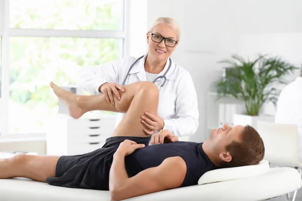 Mature doctor examining sportsman with joint pain in clinic — Stock Photo, Image