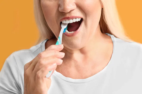 Mature woman brushing teeth on color background, closeup — Stock Photo, Image