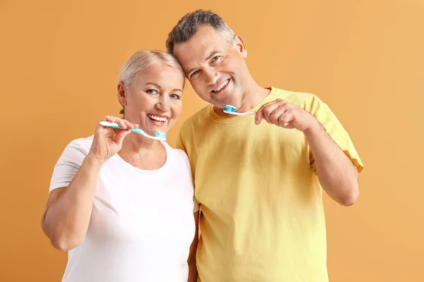 Mature couple brushing teeth on color background — Stock Photo, Image