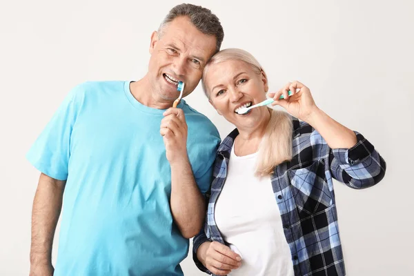 Mature couple brushing teeth on light background — Stock Photo, Image