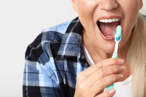 Starší žena čištění zubů na světlém pozadí, detailní záběr — Stock fotografie