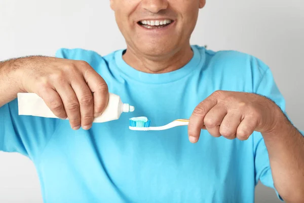 Mature man with toothbrush and paste on light background — Stock Photo, Image