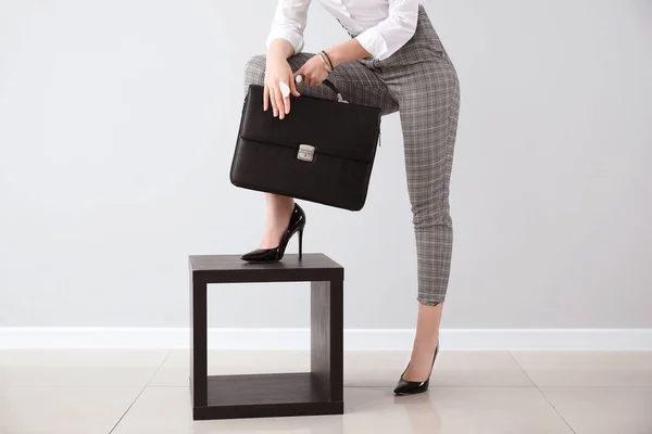 Fashionable young woman with briefcase against light wall — Stock Photo, Image