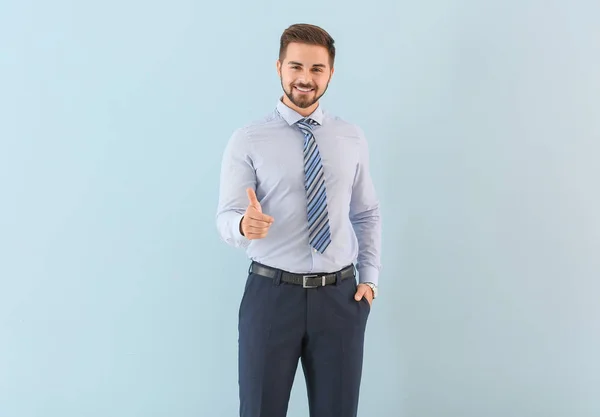 Portrait of young businessman showing thumb-up gesture on color background — Stock Photo, Image