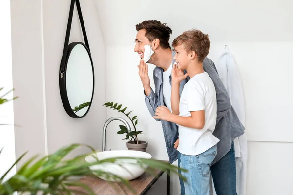 Отец с сыном наносят пену для бритья на лица в ванной комнате — стоковое фото