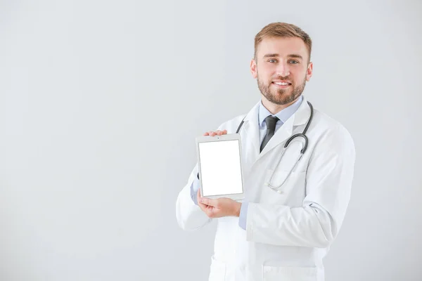 Portrait of male doctor with tablet computer on light background — 스톡 사진