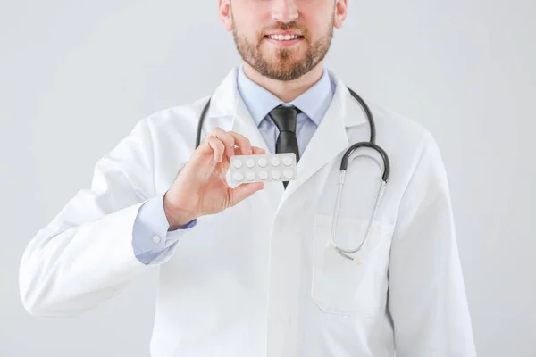 Male doctor with pills on light background