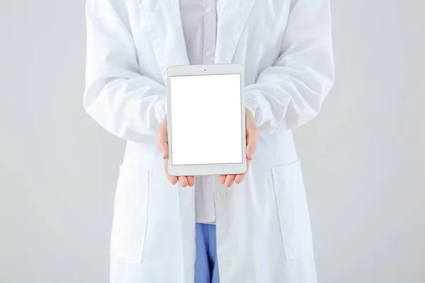 Female doctor with tablet computer on light background — Stock Photo, Image