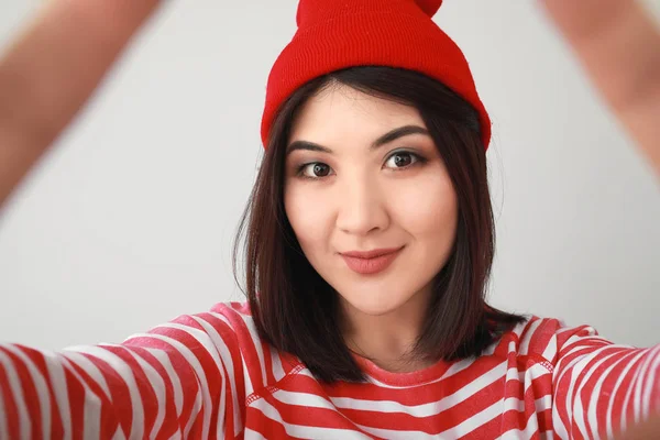 Portrait of beautiful young Asian woman taking selfie on light background — Stock Photo, Image