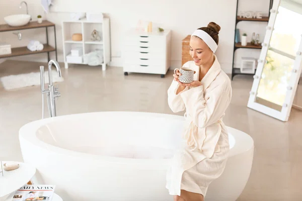 Schöne junge Frau trinkt Tee im Badezimmer — Stockfoto