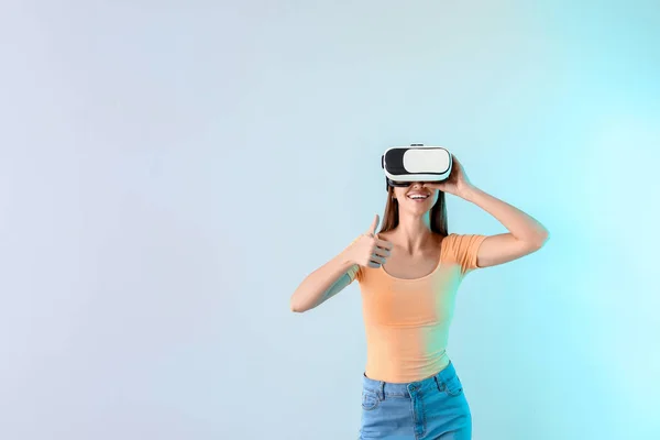 Mujer joven con gafas de realidad virtual mostrando gesto de pulgar hacia arriba sobre fondo claro — Foto de Stock