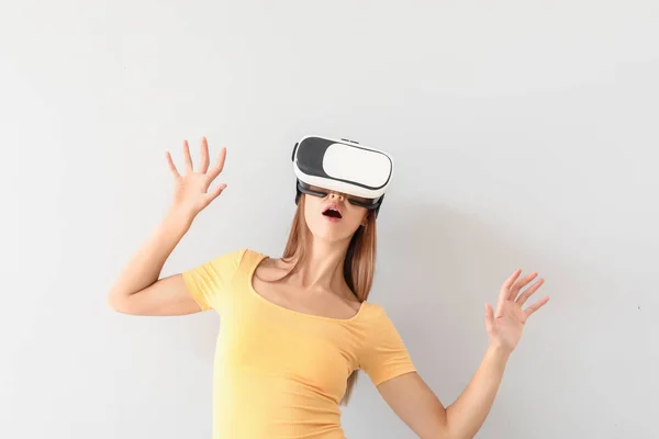 Młoda kobieta w okularach wirtualnej rzeczywistości na jasnym tle — Zdjęcie stockowe