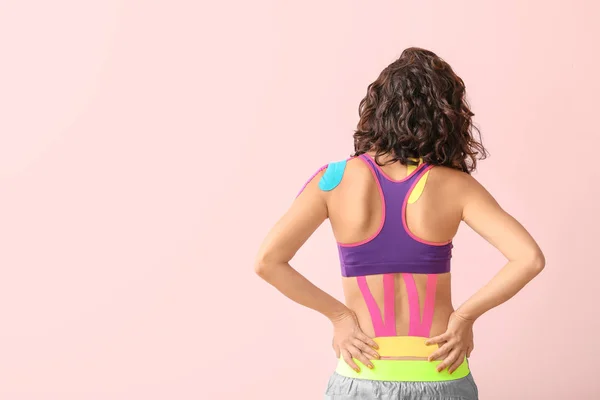 Αθλητική γυναίκα με ταινία physio εφαρμόζεται στο κάτω μέρος της πλάτης με φόντο το χρώμα — Φωτογραφία Αρχείου