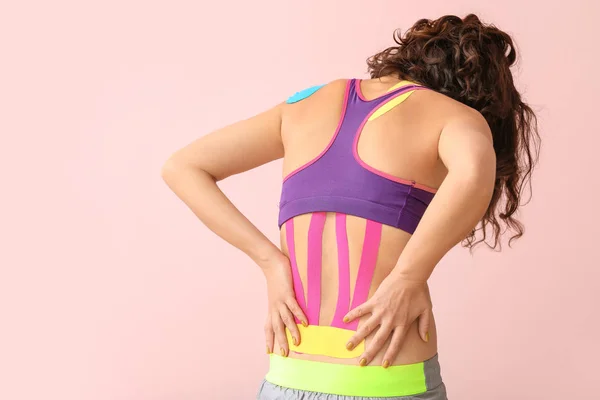 Donna sportiva con nastro fisioterapico applicato sulla parte bassa della schiena sullo sfondo di colore — Foto Stock