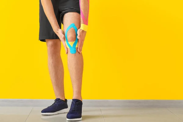 Uomo sportivo con nastro fisioterapico applicato sul ginocchio contro lo sfondo colore — Foto Stock
