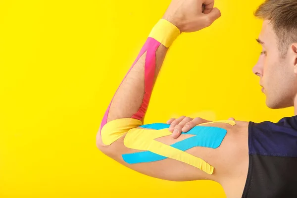 Uomo sportivo con nastro fisioterapico applicato sul braccio contro lo sfondo colore — Foto Stock