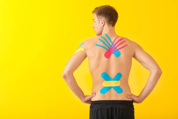 Uomo sportivo con nastro fisioterapico applicato sulla schiena contro lo sfondo colore — Foto Stock