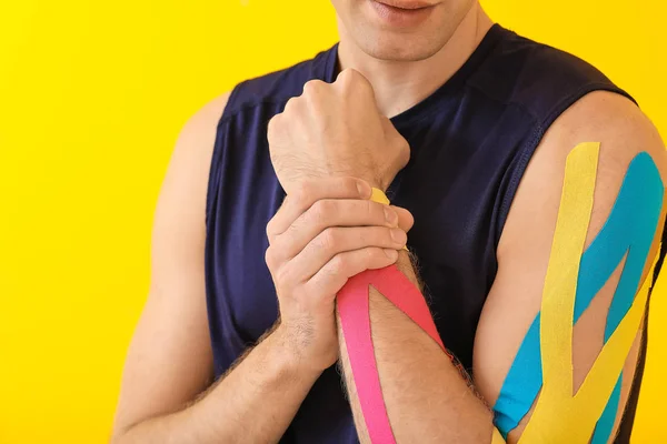Uomo sportivo con nastro fisioterapico applicato sul braccio contro lo sfondo di colore, primo piano — Foto Stock