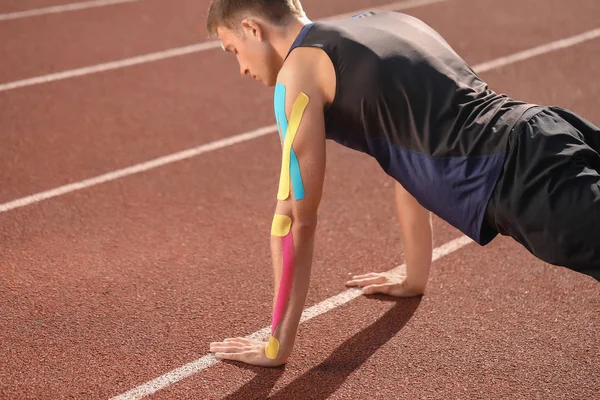 Sporty man with physio tape training at stadium — Stock Photo, Image