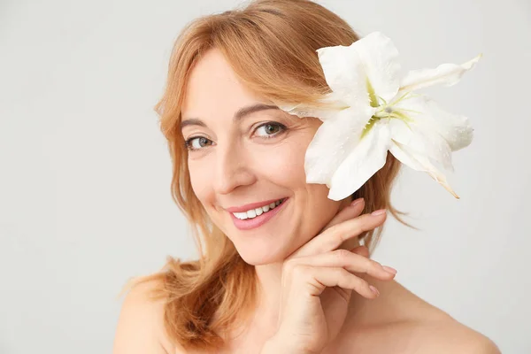 Volwassen vrouw met bloem in haar haar op lichte achtergrond — Stockfoto