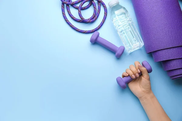 Kobieca ręka z hantlami, butelka wody i mata do jogi na tle koloru — Zdjęcie stockowe
