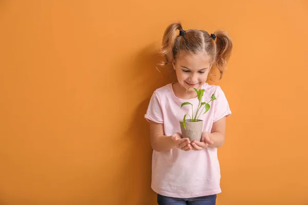Happy little girl with young plant in pot on color background — Stock Photo, Image