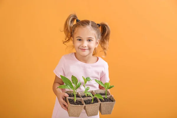 Happy little girl with young plants in pots on color background — Stock Photo, Image