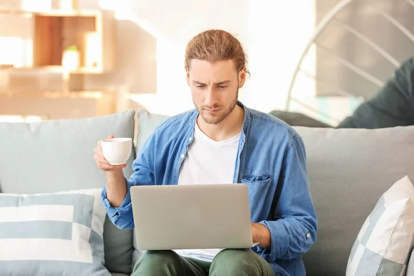 Schöner Mann mit Laptop trinkt Kaffee zu Hause — Stockfoto