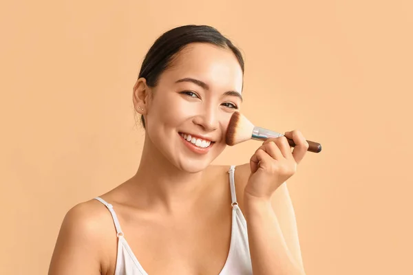 Portret van jonge Aziatische vrouw met make-up borstel op kleur achtergrond — Stockfoto