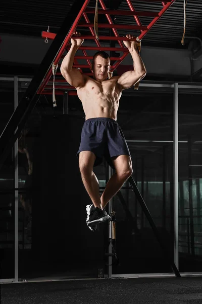 Sporty muscular man hanging on monkey bars in gym — Stock Photo, Image