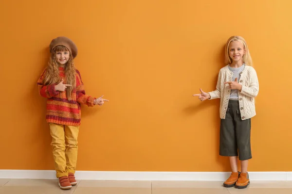 Cute little girls in autumn clothes pointing at something on color wall — Stock Photo, Image