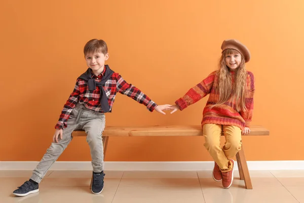 Carino bambini in abiti autunnali seduti sulla panchina vicino alla parete di colore — Foto Stock