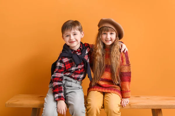 Sonbahar kıyafetleri içinde şirin çocuklar renk duvarının yanındaki bankta oturuyorlar. — Stok fotoğraf