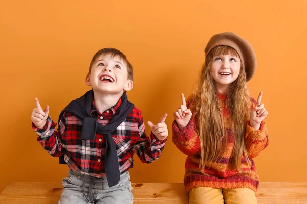 Cute little children in autumn clothes pointing at something while sitting near color wall — Stock Photo, Image