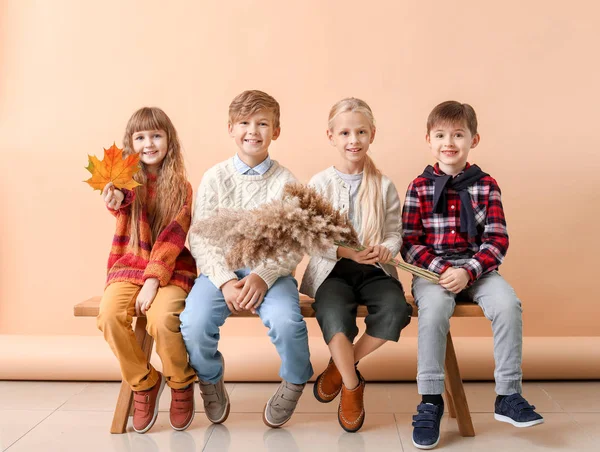 Söta små barn i höst kläder sitter på bänk nära färg vägg — Stockfoto