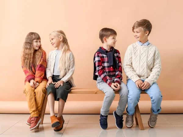 Lindos niños pequeños en ropa de otoño sentados en el banco cerca de la pared de color —  Fotos de Stock